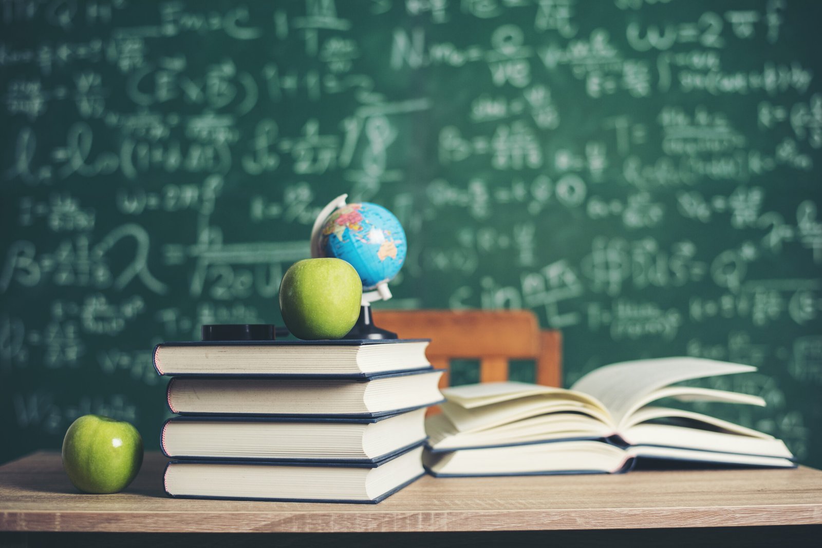 books stacked, green apple and a globe with green board background